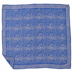 May include: A square, blue scarf with a repeating pattern of cream-colored, stylized floral and animal motifs. The scarf has a cream-colored border with a geometric design. The fabric is folded at the bottom left corner.