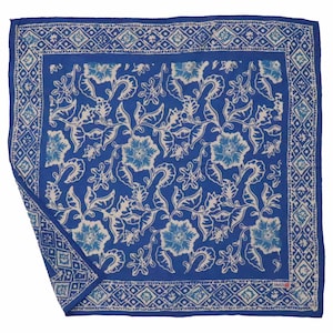 May include: A square, blue handkerchief with a floral pattern. The design features white and light blue flowers and leaves on a darker blue background. A geometric border frames the floral design.