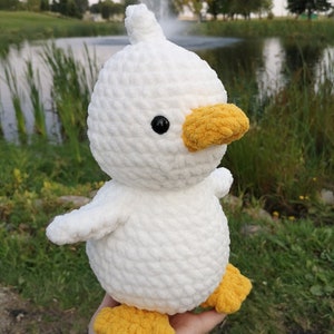 May include: White crocheted duck plush toy with yellow beak and feet. The duck has black eyes and a white fluffy body.