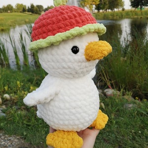 May include: White crocheted plush toy duck wearing a red and green crocheted watermelon hat.