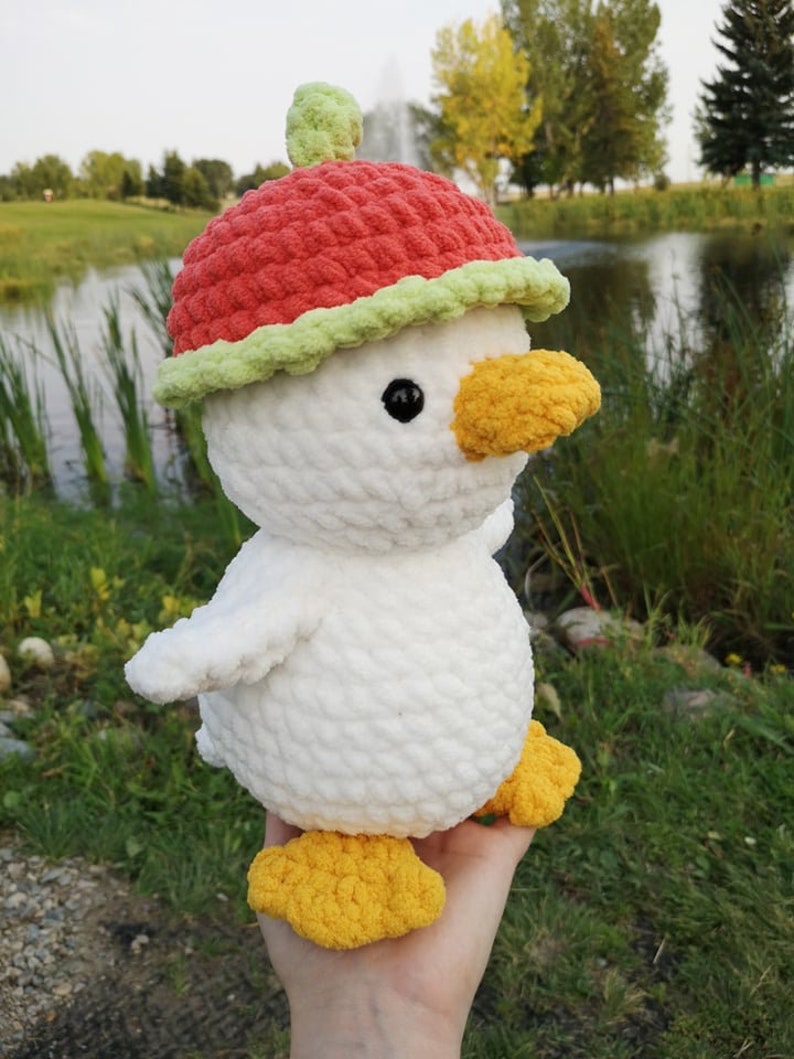 May include: White crocheted plush toy duck wearing a red and green crocheted watermelon hat.