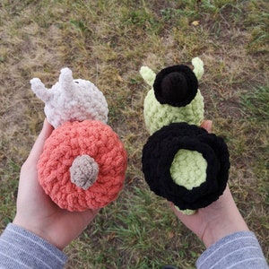 May include: Two crocheted stuffed toys, one is white with a pink body and the other is green with a black body.