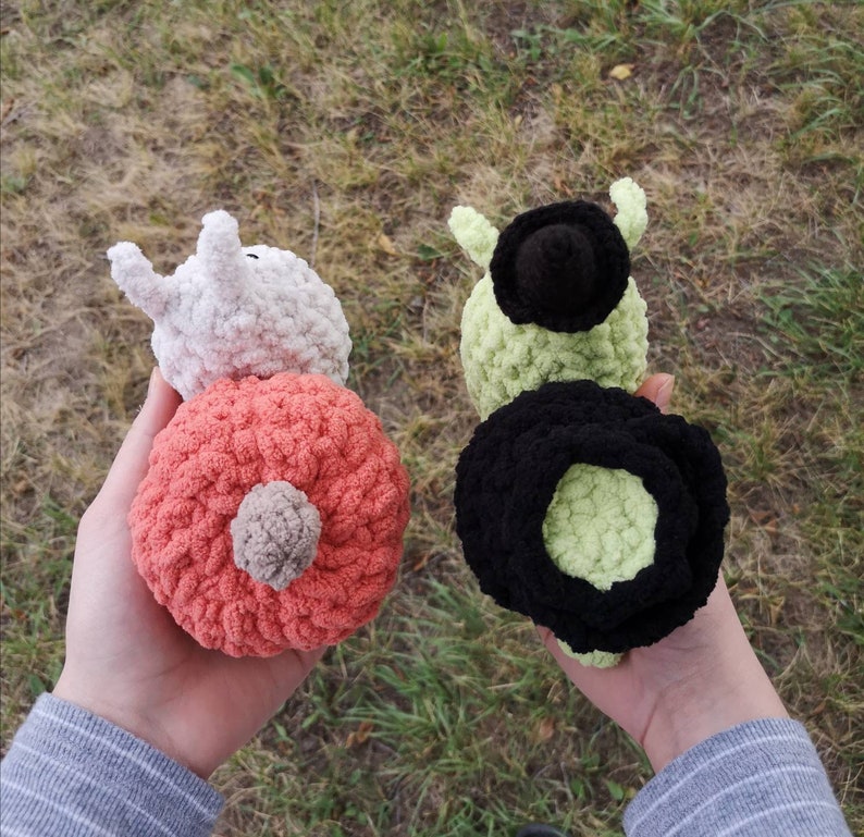 May include: Two crocheted stuffed toys, one is white with a pink body and the other is green with a black body.