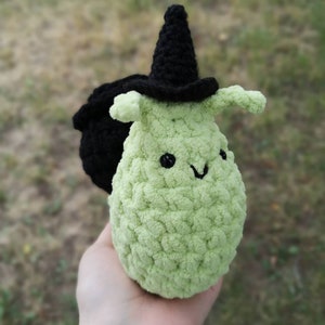 May include: A green crocheted witch with a black pointed hat and a black cauldron. The witch has a smiling face with black eyes.