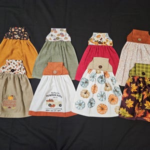 Puede incluir: Siete toallas de cocina diferentes con diseños de temática otoñal. Las toallas están hechas de un material suave y absorbente y presentan una variedad de colores, incluyendo naranja, marrón, verde y rojo. Las toallas están decoradas con calabazas, hojas y otros motivos otoñales. Una toalla tiene el texto "Fall Harvest Blessings".