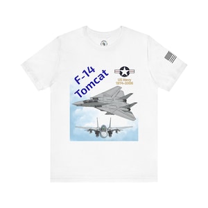 May include: White t-shirt featuring a graphic of an F-14 Tomcat fighter jet in flight, with the text "F-14 Tomcat" in blue. The shirt also includes the US Navy logo and the text "US Navy 1974-2006". A small American flag is on the sleeve.