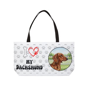 Może przedstawiać: Biała torba z czarnymi uchwytami. Zawiera ilustrację jamnika w okręgu, powtarzający się wzór łap i tekst "I ❤️ MY DACHSHUND" z kością i sercem z odcisku łapy.