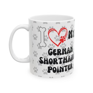 May include: White ceramic mug with a handle, featuring the text "I love my German Shorthair Pointer." The design includes a red heart with a paw print, a bone, and grey paw prints scattered across the surface.