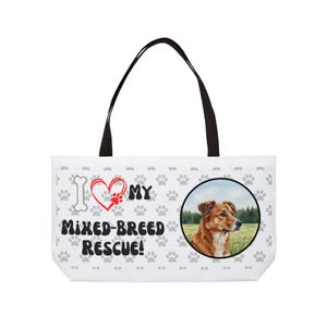Może przedstawiać: Biała torba z czarnymi uchwytami. Torba ma napis "I ❤️ MY MIXED-BREED RESCUE!" i odciski łap. Okrągły obraz brązowo-białego psa znajduje się po prawej stronie.