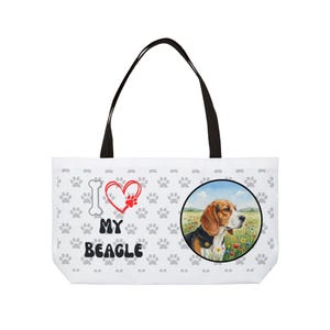 Może przedstawiać: Biała torba typu tote z czarnymi uchwytami. Zawiera ilustrację beagle w okrągłej ramce, odciski łap i napis "I ❤️ MY BEAGLE". Beagle znajduje się na polu kwiatów.