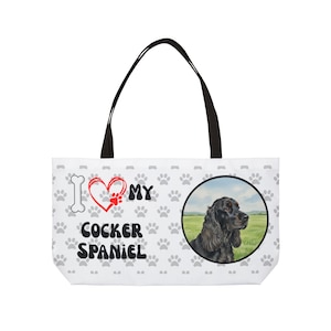 Może przedstawiać: Biała torba typu tote z czarnymi uchwytami. Zawiera ilustrację Cocker Spaniela w okrągłej ramce. Torba ma napis "I Love My Cocker Spaniel" z odciskami łap i wzorem serca.