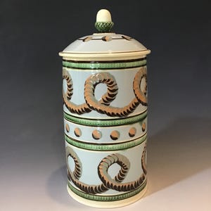 May include: A light blue ceramic jar with a lid, featuring a repeating design of brown and gray swirls. The jar has green and cream-colored bands and a white knob on top. The jar is approximately 10 inches tall.