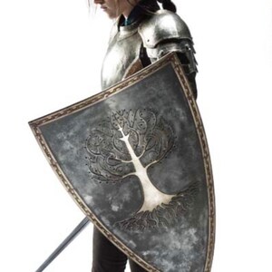 May include: A woman in silver armor holds a shield with a white tree design. She is holding a sword in her other hand.