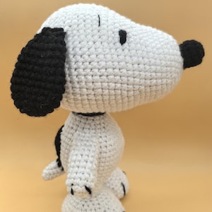 Puede incluir: Perro de peluche blanco tejido a crochet con orejas y nariz negras. El perro está de pie sobre una superficie marrón claro.