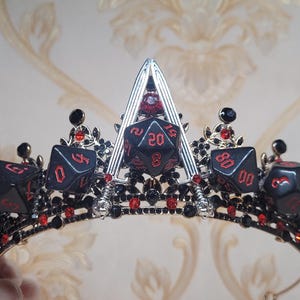 Puede incluir: Una corona negra y plateada con acentos de dados rojos. La corona est&aacute; decorada con cristales negros y rojos.