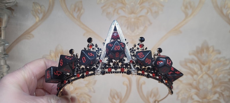 Puede incluir: Una corona negra y plateada con acentos de dados rojos. La corona est&aacute; decorada con cristales negros y rojos.