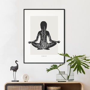Puede incluir: Una ilustraci&oacute;n en blanco y negro de una persona en una postura de yoga con la palabra "NAMASTE" impresa debajo. La ilustraci&oacute;n est&aacute; enmarcada y colgada en una pared blanca sobre un gabinete de madera con una puerta de rat&aacute;n tejido. Una figurita de p&aacute;jaro negro est&aacute; en el gabinete.