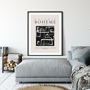 May include: A black and white minimalist art print with the text "GALERIE BOHEME" and "Evviva Parte" in a black frame. The print features a black background with white abstract lines and shapes. The text "La Galerie des Arts | tous les jours | sauf le lundi 1000-1800" is at the bottom of the print.