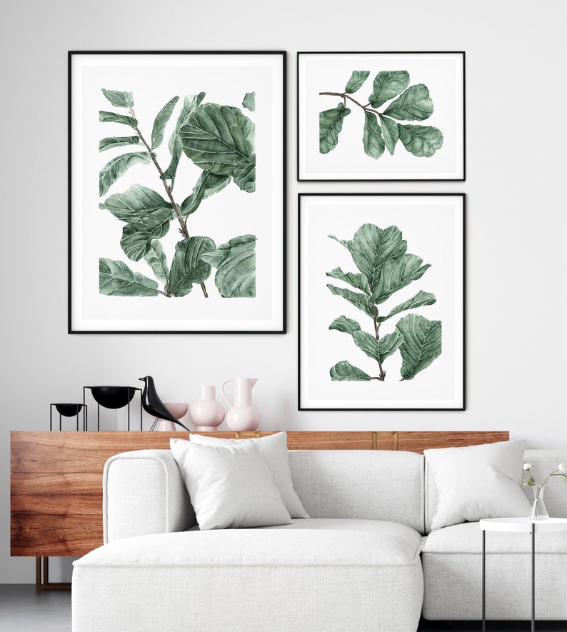 Op de afbeelding: Drie ingelijste aquarelprints van groene bladeren op een witte achtergrond. De prints zijn in een rij op een witte muur gerangschikt.