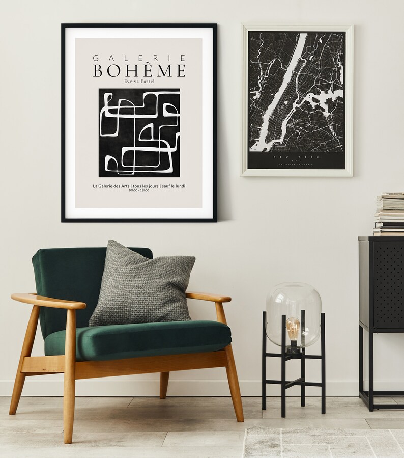 May include: A black and white abstract art print with the text "GALERIE BOHEME" and "Exviva l'arte!" in a white sans-serif font. The print is framed in black and hanging on a white wall. A green velvet armchair with a gray pillow sits in front of the print. A black metal floor lamp with a clear glass globe sits on a black metal stand next to the armchair.