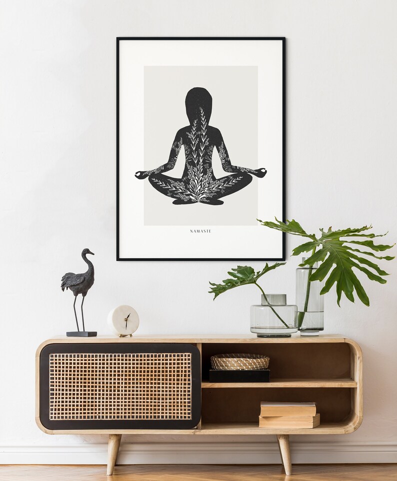 Puede incluir: Una ilustraci&oacute;n en blanco y negro de una persona en una postura de yoga con la palabra "NAMASTE" impresa debajo. La ilustraci&oacute;n est&aacute; enmarcada y colgada en una pared blanca sobre un gabinete de madera con una puerta de rat&aacute;n tejido. Una figurita de p&aacute;jaro negro est&aacute; en el gabinete.