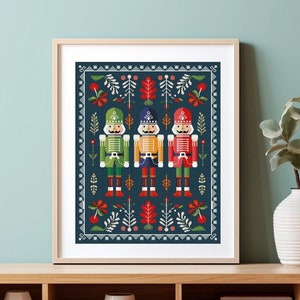 May include: Three nutcracker soldiers in green, yellow, and red stand in front of a blue background with a festive pattern of red berries, green leaves, and white flowers.
