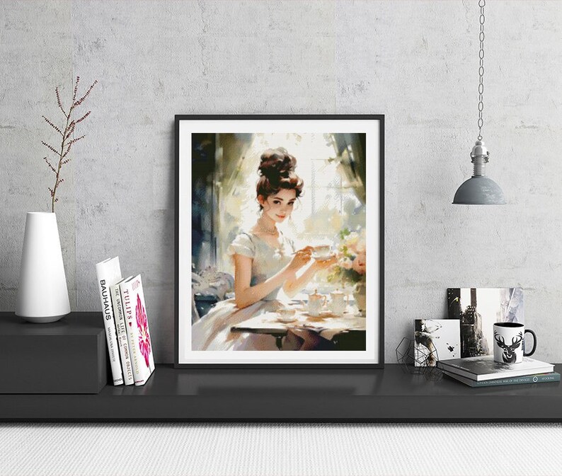 May include: A framed watercolor painting of a woman in a white dress sitting at a table with a cup of tea. The painting is set in a room with a window and sunlight streaming in.