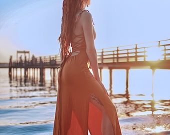 May include: A floor-length, sleeveless, burnt-orange dress featuring a high side slit and a lace-up back design with thin straps. The garment is constructed with a fitted bodice that transitions into a flowing skirt, showcasing a solid colour.