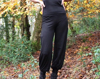 May include: A black halter top with a deep V-neckline paired with matching black loose-fitting trousers that feature gathered cuffs at the ankles and a pair of dark lace-up boots, creating a coordinated monochromatic outfit.