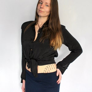 Puede incluir: Una mujer con una camisa negra abotonada atada a la cintura y una falda azul oscuro. Tiene el pelo largo y casta&ntilde;o y mira a la c&aacute;mara.