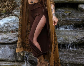 May include: A brown crop top, brown high-waisted pants with side slits, and a long, open-front mustard-colored duster cardigan featuring a dark brown geometric pattern along the edges and hem, paired with brown lace-up boots.