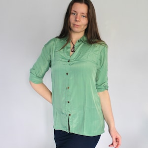 Puede incluir: Una camisa de manga larga de color verde claro con botones y cuello. La camisa est&aacute; hecha de un material sedoso y tiene un corte holgado.
