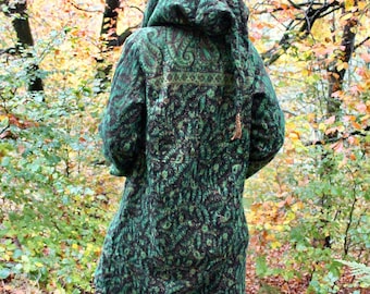 May include: A long-sleeved hooded jacket in a dark green and black paisley pattern. The garment features a large hood, a straight hemline with fringe detailing at the bottom, and a woven texture throughout the fabric.