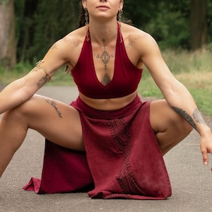 May include: A burgundy halter top and matching skirt with a decorative pattern. The outfit is worn by a person sitting on a paved road with trees in the background. The top has a deep V-neck.