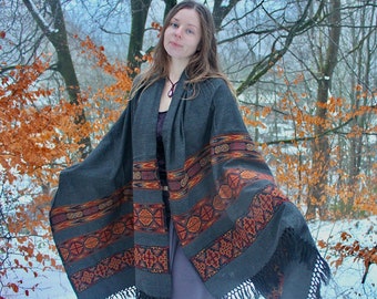 May include: A gray wool shawl with a colorful geometric pattern and fringe. The shawl is draped over a person's shoulders in a snowy forest setting.