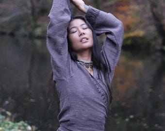 May include: A long-sleeved, dark gray wrap top featuring a V-neckline and decorative black stitching along the cuffs and front edge. The garment is paired with a plain, light-colored skirt, creating a layered ensemble with a textured fabric finish.