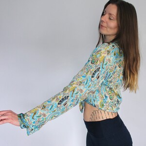 Op de afbeelding: Een vrouw draagt een blauw en wit gebloemd gewashemd met lange mouwen. Het shirt heeft een paisley-ontwerp. De vrouw draagt een donkerblauwe rok.