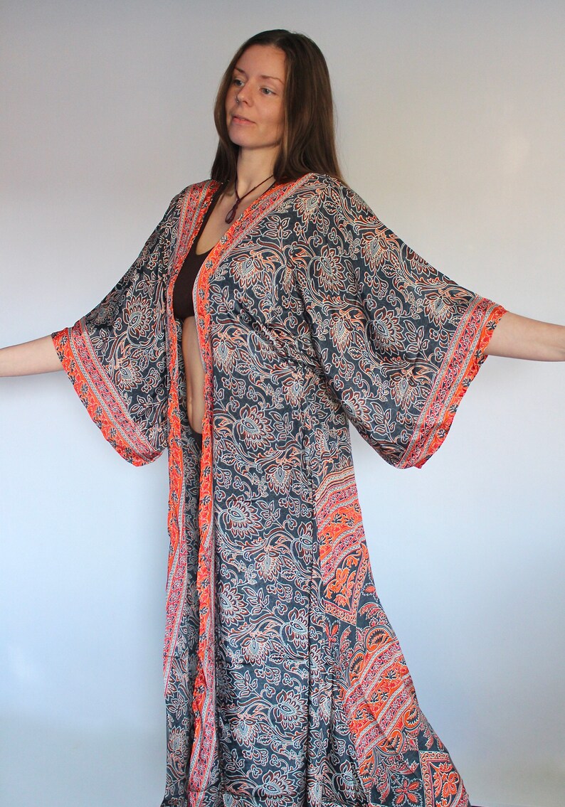 May include: A long, flowing, black and orange patterned kimono with a floral design. The kimono has long sleeves and a wide, open neckline.