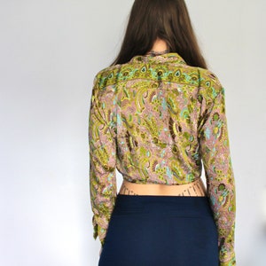 Op de afbeelding: Een lang mouw, getailleerd blouse met een paisley print in tinten van groen, bruin en roze. De blouse heeft een wikkel sluiting en een aansluitende pasvorm.