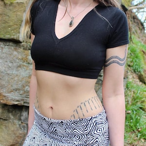 May include: A black short-sleeved crop top with a deep V-neckline paired with a skirt featuring a black and white geometric diamond pattern. The top is fitted and ends above the waist, while the skirt has a wide waistband and a repeating print.
