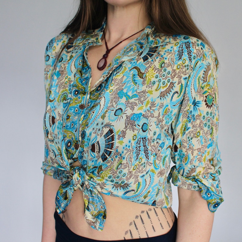 Op de afbeelding: Een blauw en wit paisley-print overhemd met een bruine bies. Het overhemd is in de taille geknoopt en heeft lange mouwen.