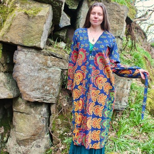 May include: A long, blue and orange patterned robe with a V-neck and long sleeves. The robe is tied at the waist with a matching fabric belt.