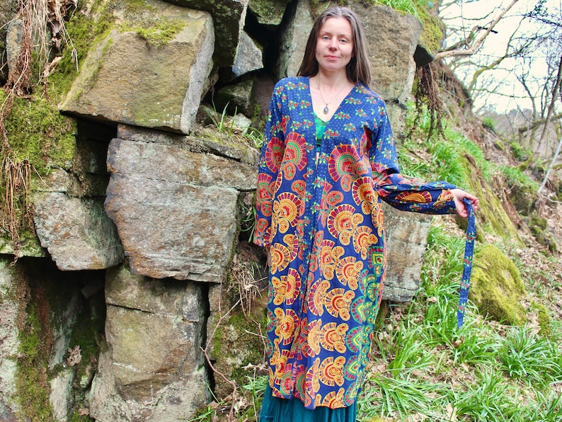May include: A long, blue and orange patterned robe with a V-neck and long sleeves. The robe is tied at the waist with a matching fabric belt.