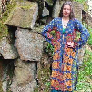 May include: A long, blue and orange patterned kimono with a tie closure. The kimono has a floral design with a paisley pattern. The model is wearing the kimono with a green top underneath.