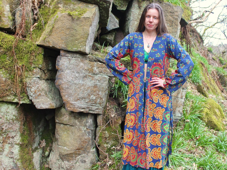 May include: A long, blue and orange patterned kimono with a tie closure. The kimono has a floral design with a paisley pattern. The model is wearing the kimono with a green top underneath.