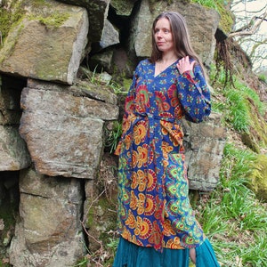 May include: A long, blue and orange patterned robe with a tie belt. The robe is made of a soft, flowing fabric and has a relaxed fit. The model is standing in a forest setting.
