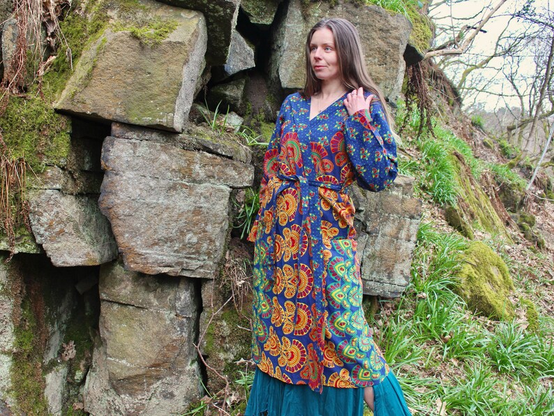 May include: A long, blue and orange patterned robe with a tie belt. The robe is made of a soft, flowing fabric and has a relaxed fit. The model is standing in a forest setting.