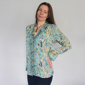 Op de afbeelding: Een lang mouw, blauw en wit gepatroneerd overhemd met een knoopsluiting en een kraag. Het overhemd heeft een paisley-ontwerp met een bruine ketting.