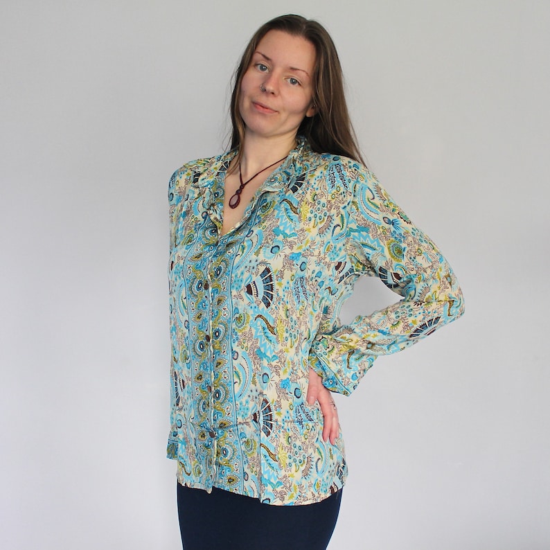 Op de afbeelding: Een lang mouw, blauw en wit gepatroneerd overhemd met een knoopsluiting en een kraag. Het overhemd heeft een paisley-ontwerp met een bruine ketting.