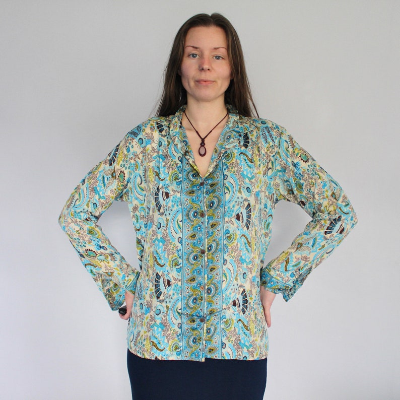 Op de afbeelding: Een lang mouw, lichtblauw shirt met een paisley-patroon. Het shirt heeft een knoopsluiting aan de voorkant en een kraag. Het shirt is gemaakt van een zachte, vloeiende stof.